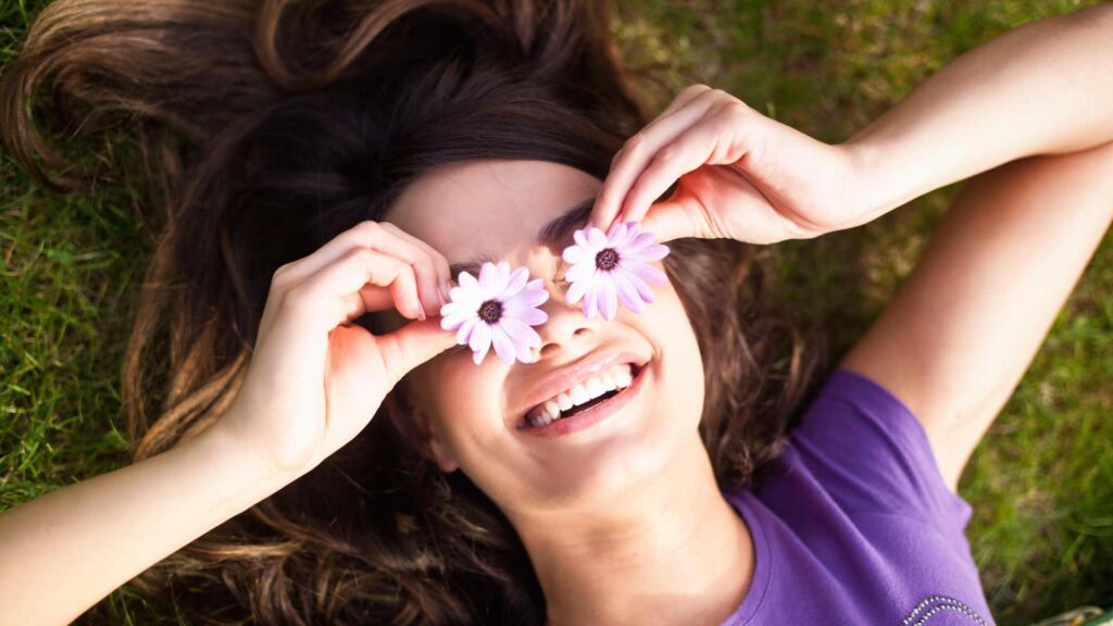 femme qui sourit avec des fleurs devant les yeux